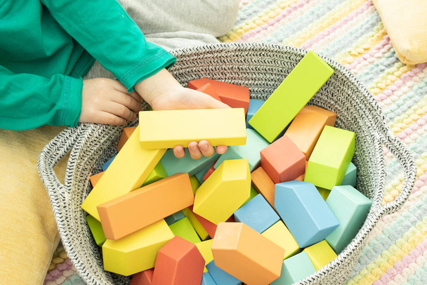 ořezané foto dítě hraje s barevnými dřevěnými bloky v košíku doma - Fotografie, Obrázek