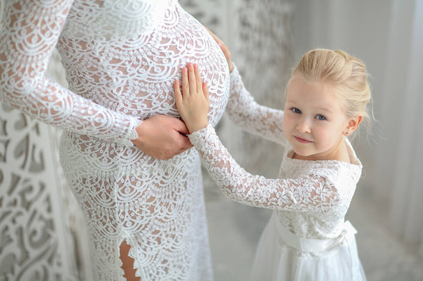 cute blonde girl in lace dress listens to mom's pregnant belly - Zdjęcie, obraz