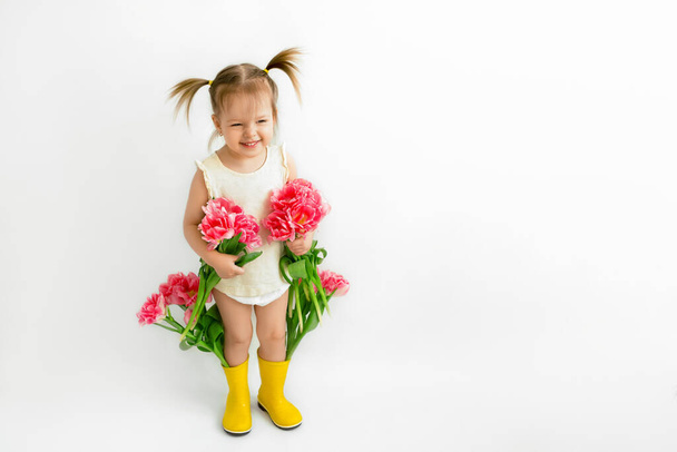 Egy lány sárga gumicsizmában egy csokor tulipánt tart a kezében. Boldog baba egy csokor virággal anyának.. - Fotó, kép