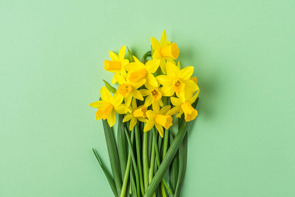 Ramo de flores narcisas amarillo primavera sobre fondo verde pastel. concepto de Pascua feliz. Vista superior. plano laico - Foto, imagen