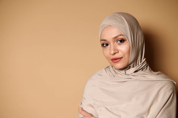 Retrato confiante de uma mulher muçulmana árabe serena e bonita em hijab e traje conservador rigoroso. Fechar em fundo bege com espaço de cópia - Foto, Imagem