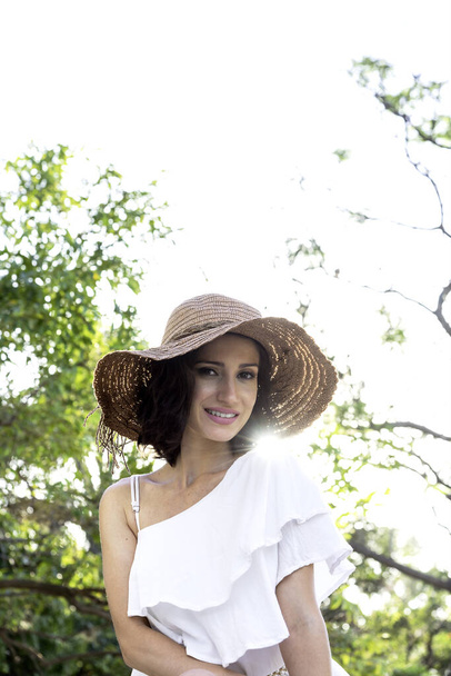 Ontspannen en gelukkige vrouw in het park, met een grote glimlach tegen de lichte witte hoed - Foto, afbeelding