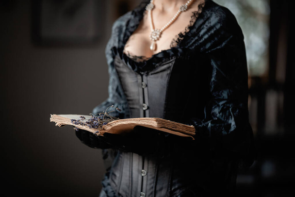 Bella donna in abito nero che tiene un libro e fiori di lavanda al coperto - Foto, immagini