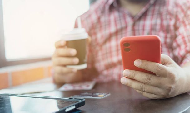 close-up handen houden koffie papieren beker en smartphone tijdens het zitten in de coffeeshop. Zakenman die koffie drinkt en lacht. Freelancer werkt en controleert e-mail en chatten met de klant. handelaar - Foto, afbeelding