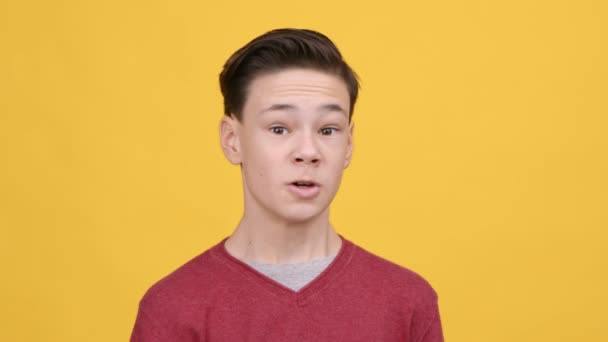 Enojado adolescente chico sacudiendo puño en amenazante gesto, fondo amarillo - Imágenes, Vídeo