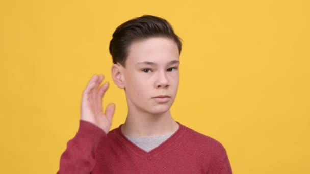 Teenager αγόρι ακούγοντας κρατώντας το χέρι κοντά στο αυτί πάνω από κίτρινο φόντο - Πλάνα, βίντεο