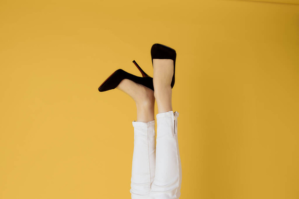 Kadınların ters dönmüş siyah ayakkabıları moda sarı arka plan - Fotoğraf, Görsel
