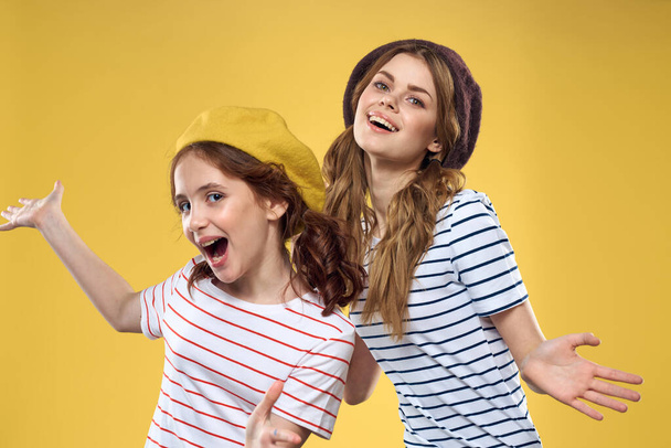 Χαρούμενες αδελφές με καπέλα ριγέ T-shirts χαρά τρόπο ζωής κίτρινο φόντο οικογένεια - Φωτογραφία, εικόνα
