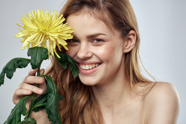 Retrato de una hermosa mujer con una flor amarilla sobre un fondo claro encantadora sonrisa modelo pelo rojo - Foto, Imagen