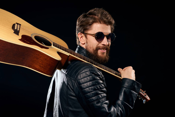 Человек с гитарой в руках кожаная куртка музыкальное исполнение рок-звезда современный стиль темный фон - Фото, изображение