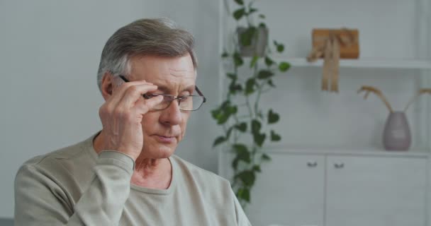 Oude gefocuste man grijs-harige grootvader zit in huis interieur leesboek draagt bril voelt ongemak pijn in de ogen lijdt aan overwerk vermoeidheid neemt af bril, visie verlies concept - Video