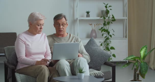 Focalisé vieux couple retraité mature famille parlant à l'aide d'un ordinateur portable moderne faire des achats sur Internet choisir de lire les nouvelles bancaires en ligne en regardant l'écran d'ordinateur assis à la maison confortable, concept de réduction de vente - Séquence, vidéo