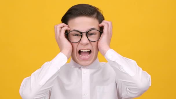 Hullu koulupoika huutaa vihassa koskettava pää yli keltainen tausta - Materiaali, video