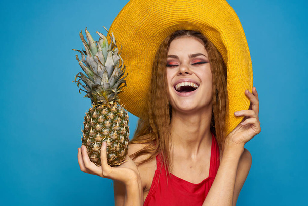 Frau mit gelbem Hut mit Ananas in den Händen Emotionen Spaß Lifestyle Sommer Obst blauer Hintergrund - Foto, Bild