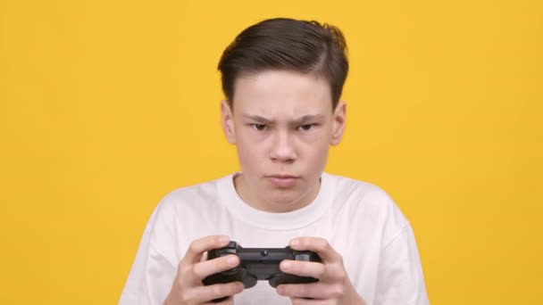 Nastolatek chłopiec gra wideo gospodarstwa Gamepad kontrolera na żółtym tle - Materiał filmowy, wideo