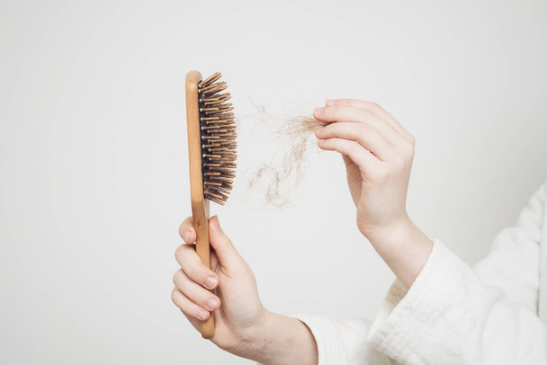 kobieta usuwa bułkę włosów z drewnianym grzebieniem na lekkim tle problemy zdrowotne utrata - Zdjęcie, obraz