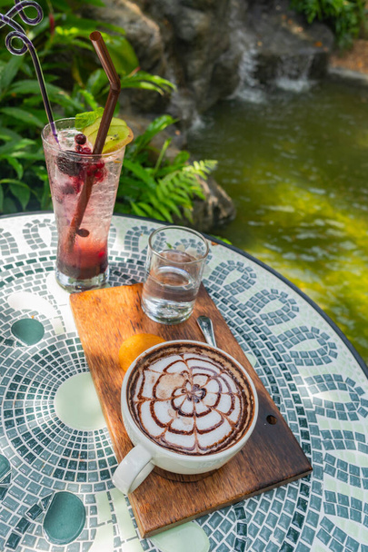 Un conjunto de bebidas calientes colocadas en una mesa de cerámica. El telón de fondo de una cascada, exuberante vegetación y vapor flotaron para que pareciera fresca - Foto, Imagen