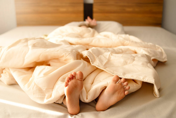 Les pieds de bébé jettent un coup d'oeil sous la couverture. Les jambes des filles sortent du lit dans un hôtel ou à la maison. - Photo, image