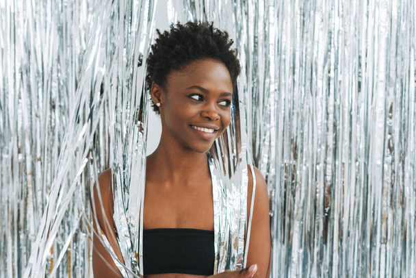 Retrato de feliz hermosa joven afroamericana en top negro sobre fondo plateado brillante, tiempo de fiesta - Foto, imagen