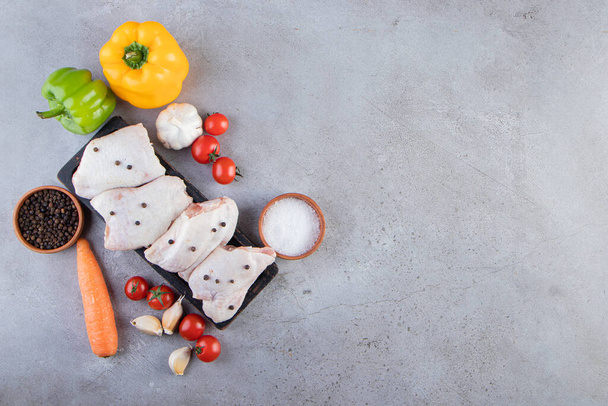 rauwe kip, specerijen en rijpe tomaten op grijze keukentafel - Foto, afbeelding