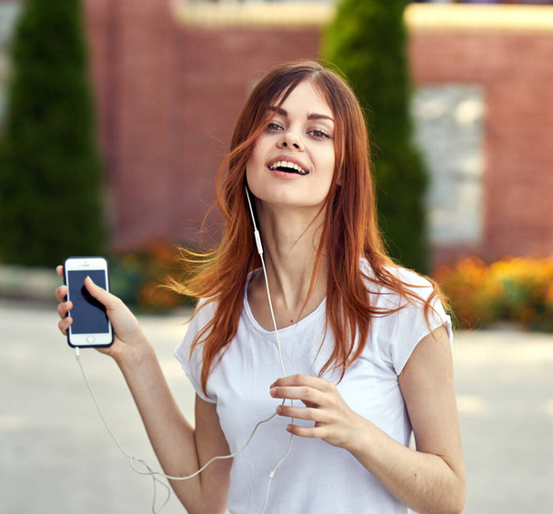 pretty woman with phone in hands outdoors with headphones on the street - Фото, изображение