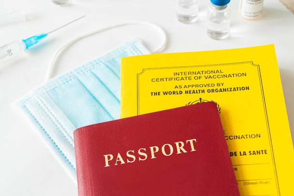 ワクチンの国際証明書を作成しました。文書は黄色です。外国人のパスポートと注射器がテーブルの上に。安全な旅行という概念は. - 写真・画像