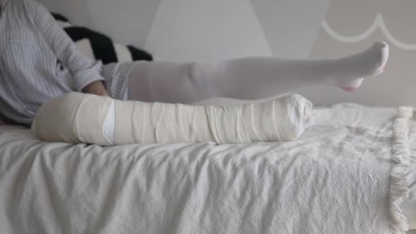 Una mujer con una pierna rota en yeso hace ejercicios para mantener su pierna tonificada - Imágenes, Vídeo