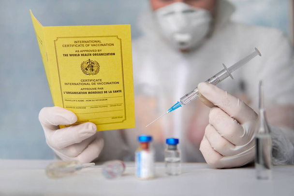 διεθνές πιστοποιητικό εμβολιασμού έγγραφο για την καταγραφή των εμβολίων που έχουν πραγματοποιηθεί. Το έγγραφο είναι ένα κίτρινο χρώμα. διαβατήριο αλλοδαπού πολίτη και μια σύριγγα στο τραπέζι. έννοια της ασφαλούς μετακίνησης. - Φωτογραφία, εικόνα