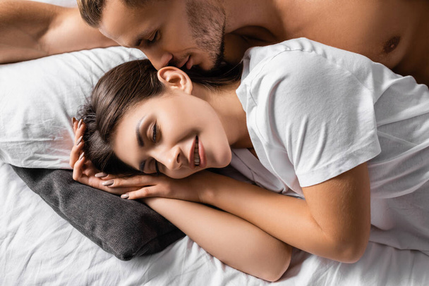 Muskulöser Mann liegt neben lächelnder Freundin mit geschlossenen Augen auf Bett  - Foto, Bild