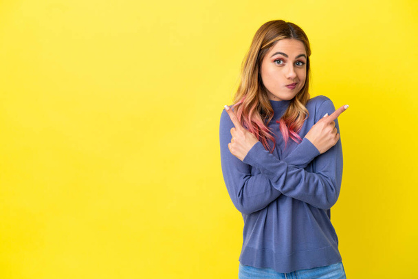 Young woman over isolated yellow background pointing to the laterals having doubts - Photo, Image