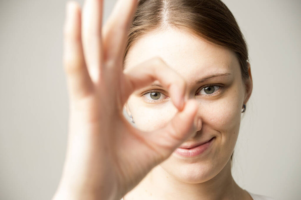 Jeune femme ayant un regard heureux, souriant, gestuel, montrant signe OK. Femme caucasienne montrant OK-geste avec ses doigts. Concept de langage corporel - Photo, image