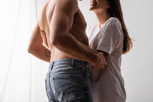 Vista recortada de la mujer sonriente en camiseta abrazando novio sexy en casa  - Foto, imagen