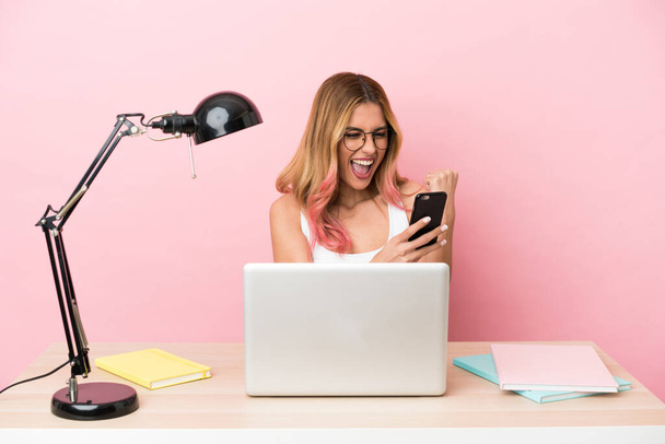 Mladá studentka na pracovišti s notebookem přes růžové pozadí překvapen a posílání zprávy - Fotografie, Obrázek