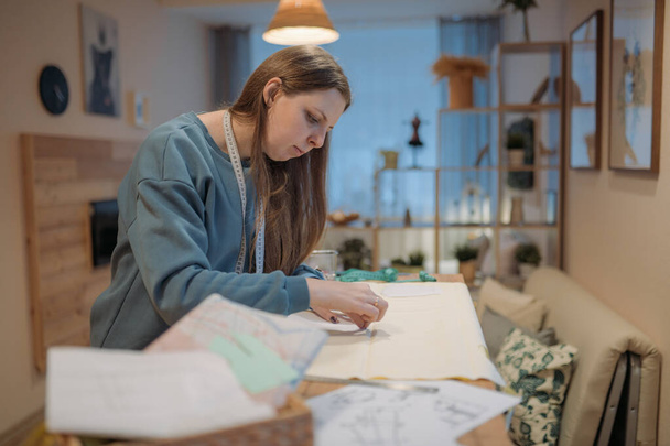 Nuori nainen siirtää kuvion ompelukankaaseen. Ompelija töissä ompelutyöpajassa kotona, harrastus kuten työ - Valokuva, kuva