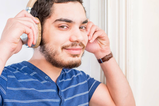 A young Caucasian man with a beard listening to music with wireless headphones and smiling - Foto, afbeelding