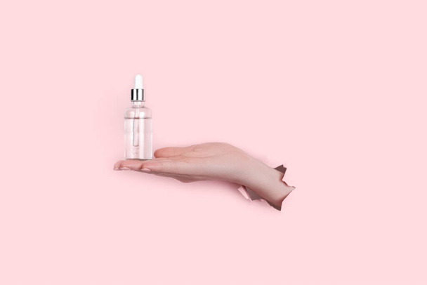 Μπουκαλάκι γυάλινο σε γυναικείο χέρι με υγρό κολλαγόνο και υαλουρονικό οξύ, ενυδάτωση δέρματος. Copyspace Αφηρημένο ροζ φόντο - Φωτογραφία, εικόνα