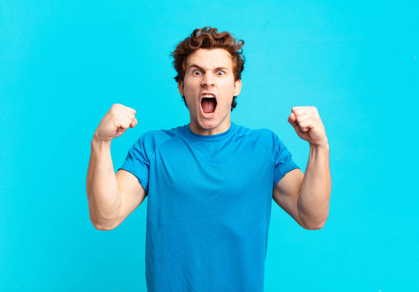 young sport boy shouting aggressively with an angry expression or with fists clenched celebrating success - Foto, immagini