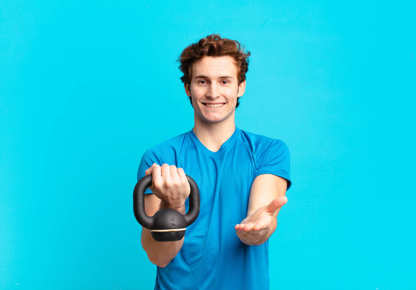 young sport boy smiling happily with friendly, confident, positive look, offering and showing an object or concept. dumbbell concept - Фото, зображення