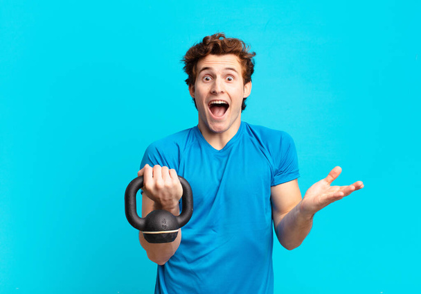 young sport boy feeling happy, excited, surprised or shocked, smiling and astonished at something unbelievable. dumbbell concept - Фото, зображення