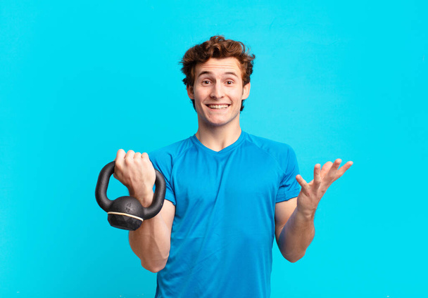 young sport boy feeling happy, surprised and cheerful, smiling with positive attitude, realizing a solution or idea. dumbbell concept - Фото, изображение