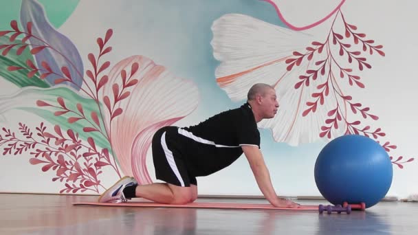 un uomo in palestra su un tappeto che fa esercizi per allungare i muscoli della schiena in una deflessione - Filmati, video