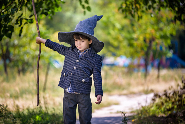 Хлопчик Тоддлер у загостреному капелюсі грає з чарівною паличкою на відкритому повітрі. Маленький чарівник. концепція Хеллоуїна
. - Фото, зображення