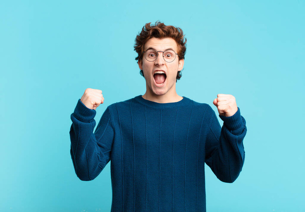 young handsome boy shouting aggressively with an angry expression or with fists clenched celebrating success - Foto, Imagen