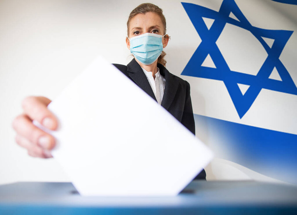 Israelin vaalit. Nainen maski laittaa hänen äänensä vaaliuurnilla - Valokuva, kuva
