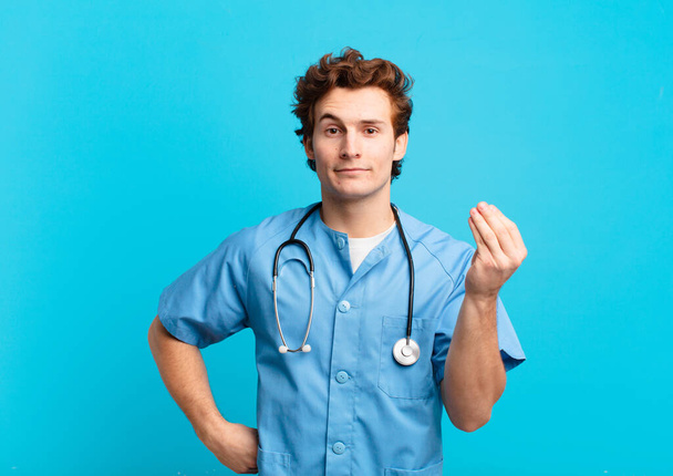 young nurse man making capice or money gesture, telling you to pay your debts! - Фото, изображение