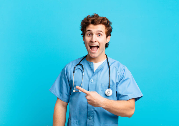 young nurse man looking excited and surprised pointing to the side and upwards to copy space - Foto, immagini