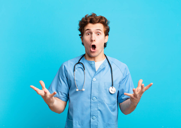 young nurse man open-mouthed and amazed, shocked and astonished with an unbelievable surprise - Φωτογραφία, εικόνα