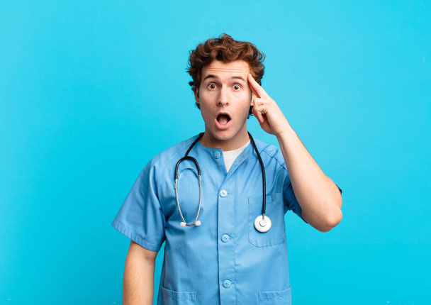young nurse man looking surprised, open-mouthed, shocked, realizing a new thought, idea or concept - Zdjęcie, obraz