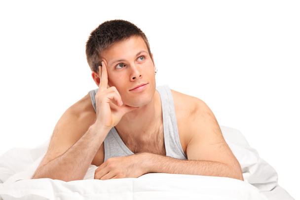 Thoughtful male lying on bed - Фото, изображение