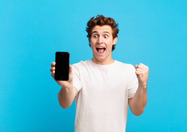 young boy feeling shocked, excited and happy, laughing and celebrating success, saying wow!. telephone screen concept - Photo, Image